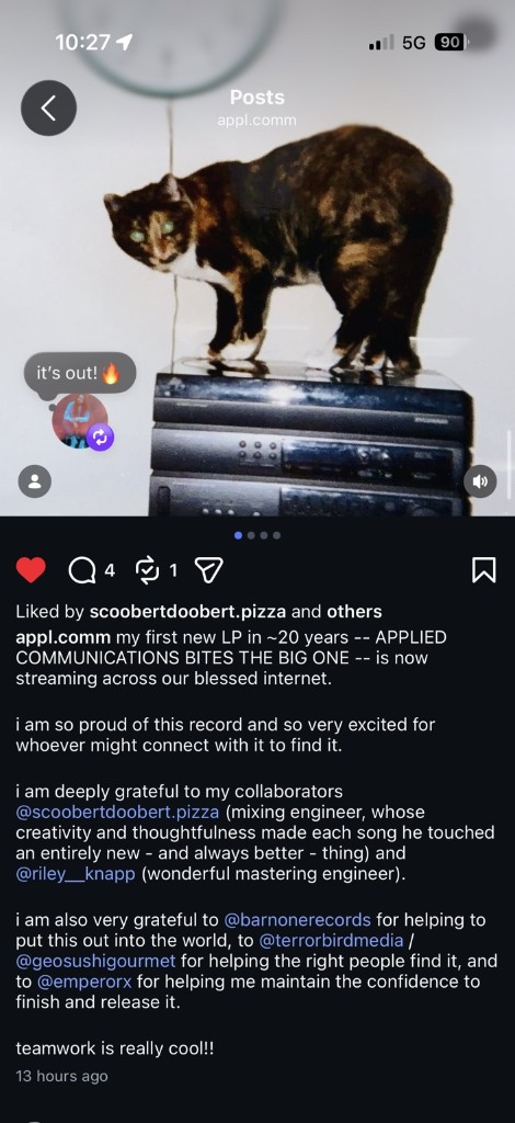 Instagram post from appl.comm, September 25, 2026: a tortoiseshell cat on a stack of VCRs under a wall clock, sticker “it’s out!”, caption naming scoobertdoobert.pizza mixing engineer and riley__knapp mastering engineer on APPLIED COMMUNICATIONS BITES THE BIG ONE.